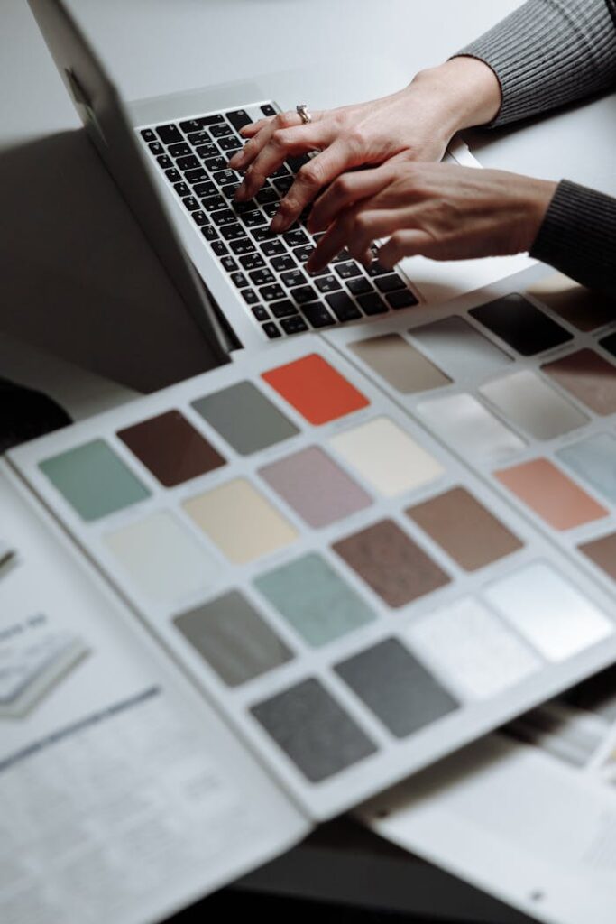 Hands typing on a laptop next to a color swatch book, ideal for design and creativity themes.